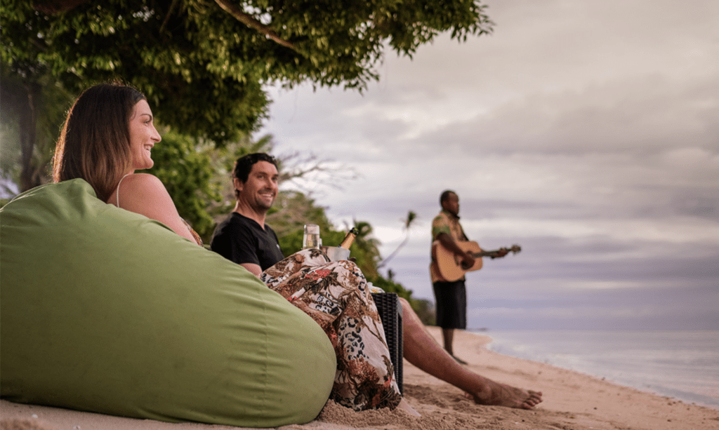 Couple relaxing on the beach, enjoying live music and a bottle of champagne.