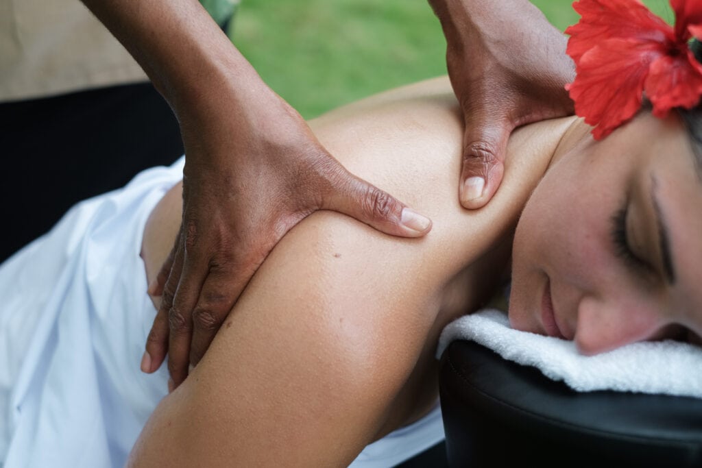 Close-up of a woman receiving a shoulder massage with a red hibiscus flower.