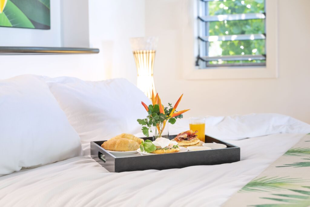 Breakfast tray on bed with croissants, juice, and eggs.