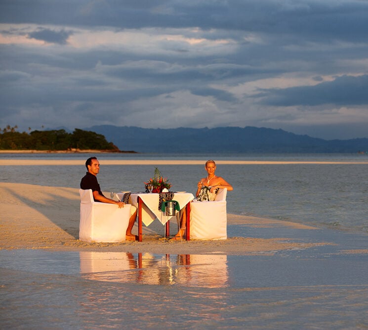Couple enjoying romantic beachside dining on a sandbar at sunset.
