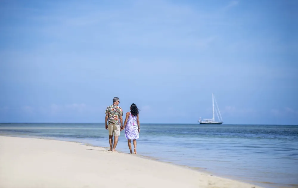 Couple walking hand-in-hand on a beach at sunset.
