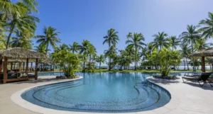 Lagoon-style pool surrounded by palm trees and thatched cabanas at Lomani Island Resort & Spa, Fiji